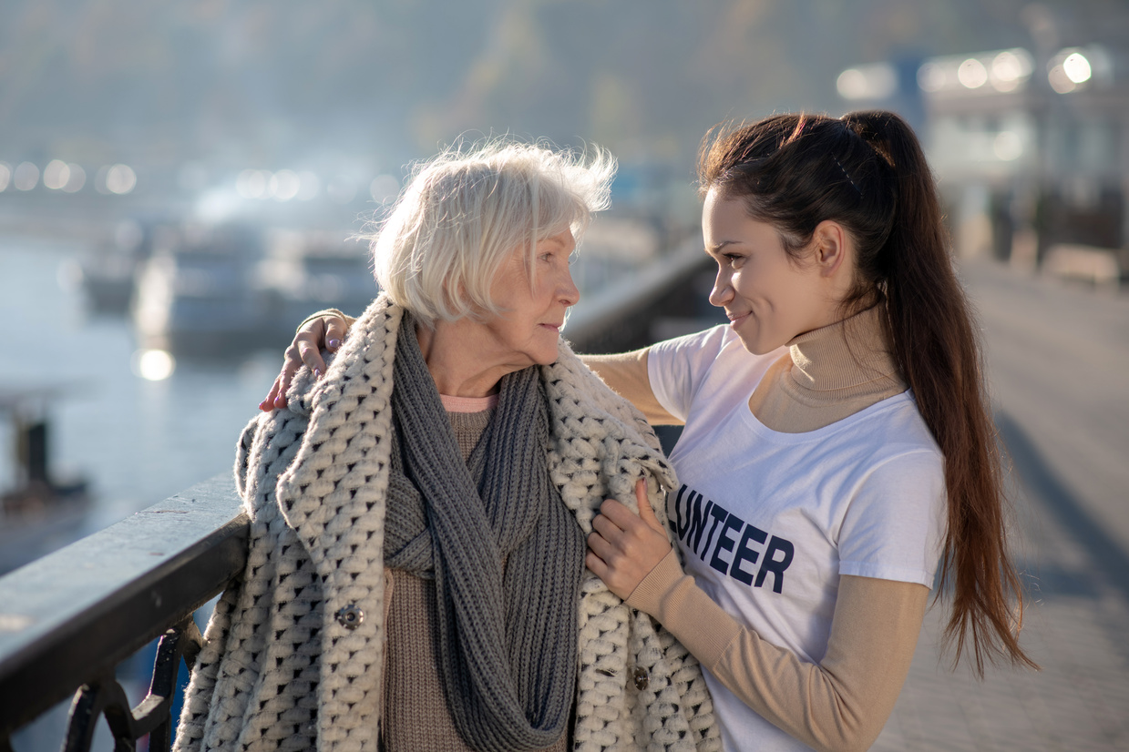 Kind volunteer smiling and hugging poor homeless pensioner